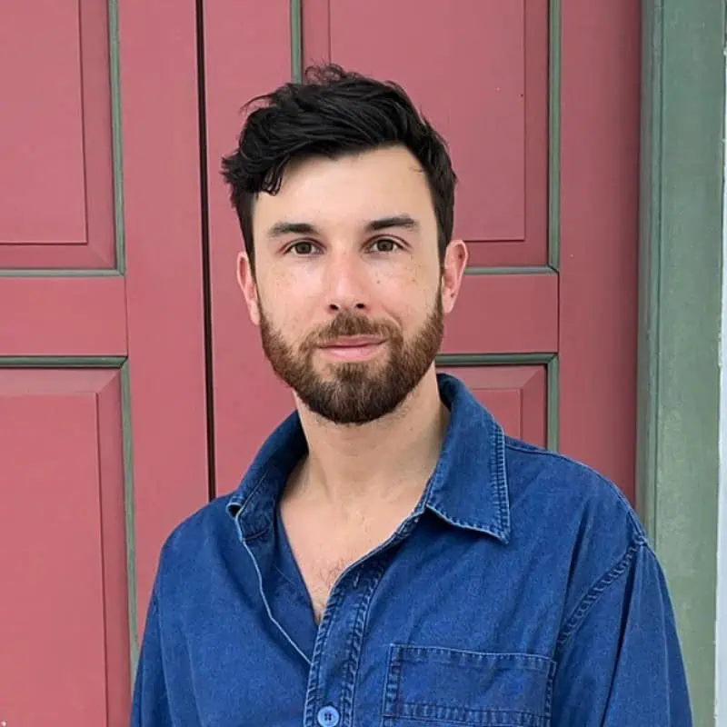 Male model with beard in casual denim shirt standing outdoors.